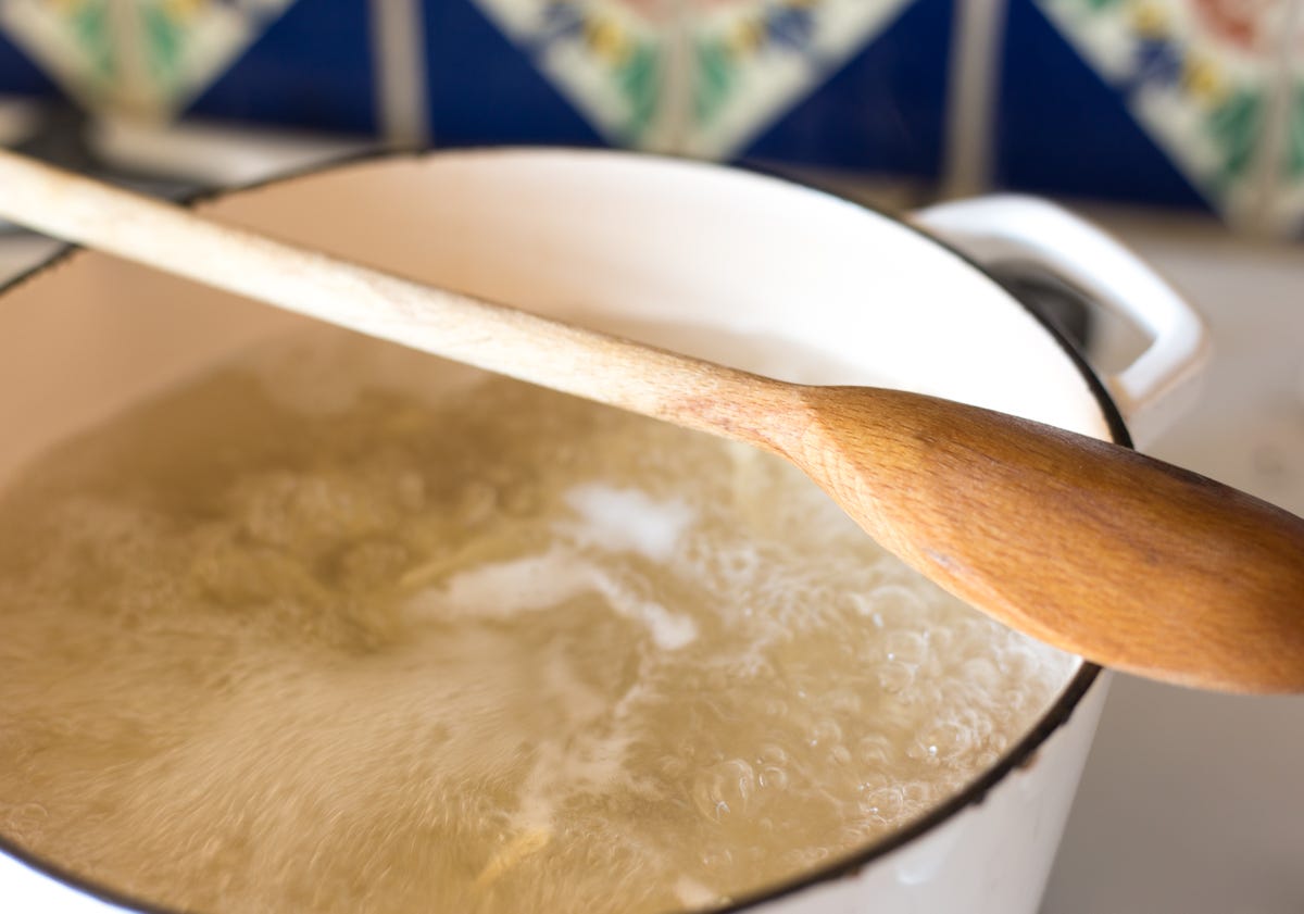 a wooden spoon over a pot of boiling water with the pasta